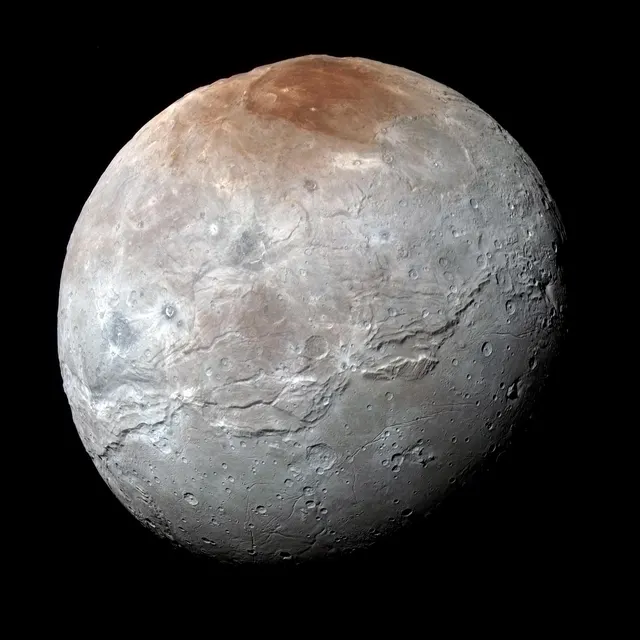 Charon in enhanced colour, grey with a reddish cap at its north pole, photographed by New Horizons