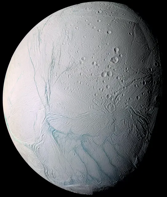 Encélado, una luna blanca y brillante con franjas azuladas cerca del polo sur, en un mosaico de Cassini